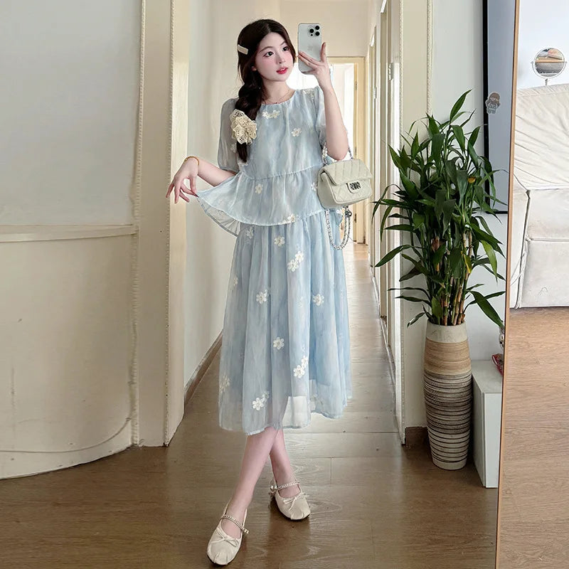 Woman in a light blue dress with floral patterns taking a mirror selfie in a room.