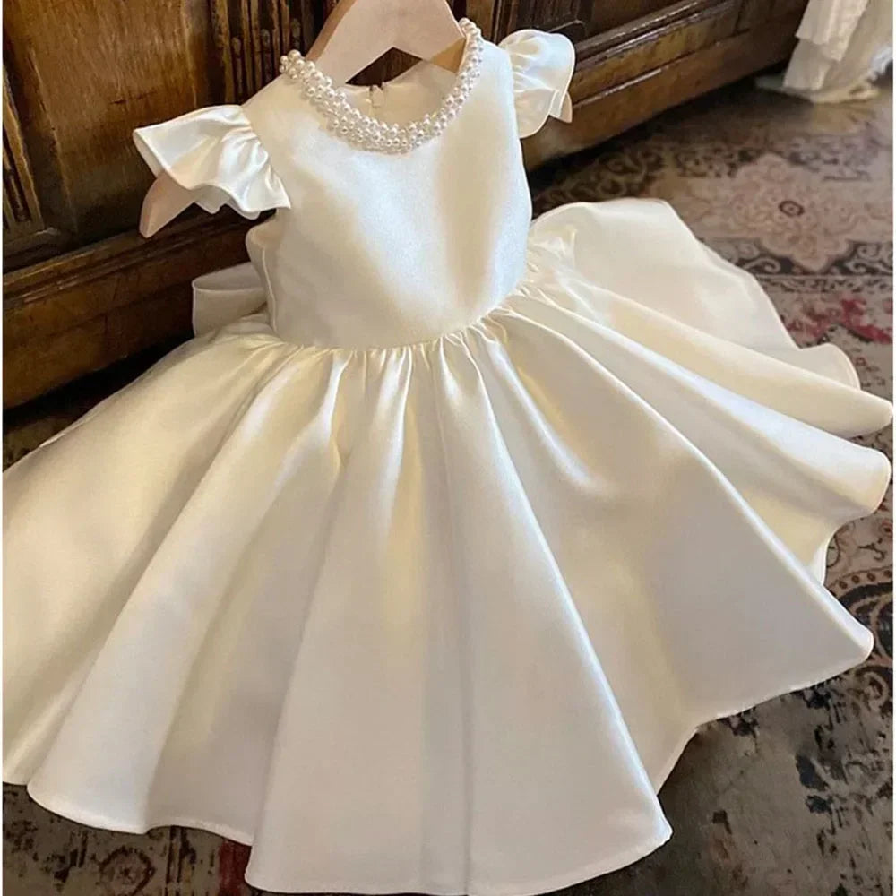 White children's dress with a bow on a wooden surface