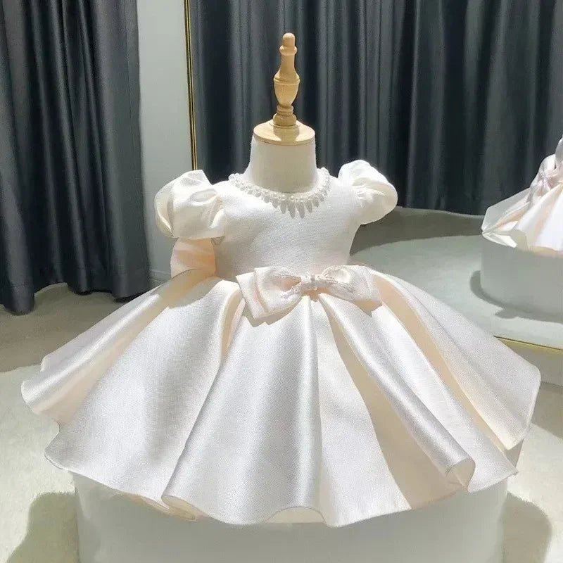 White children's dress on a mannequin against a dark curtain background