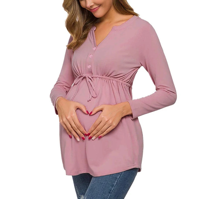 Woman wearing a pink long-sleeve top with a tie waist, holding her pregnant belly.