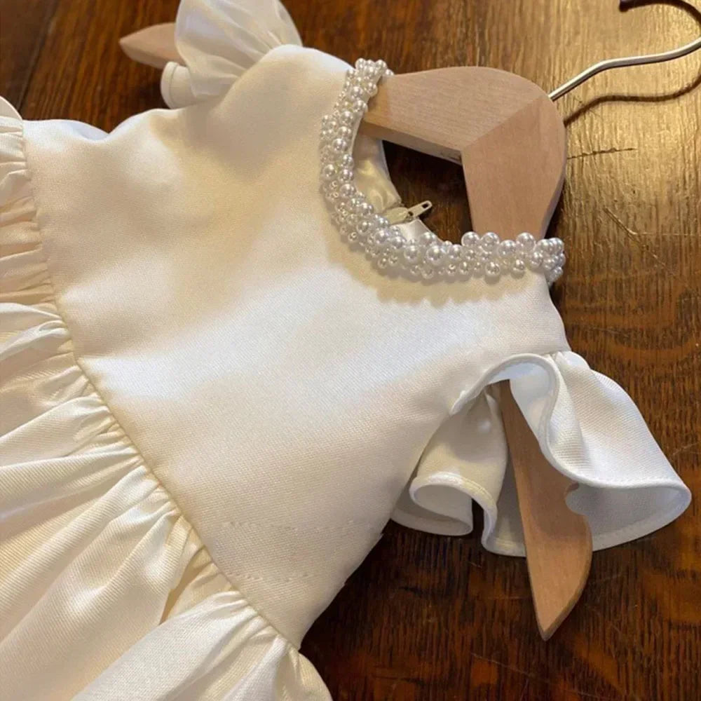 White dress on a wooden hanger with pearl details on a wooden surface