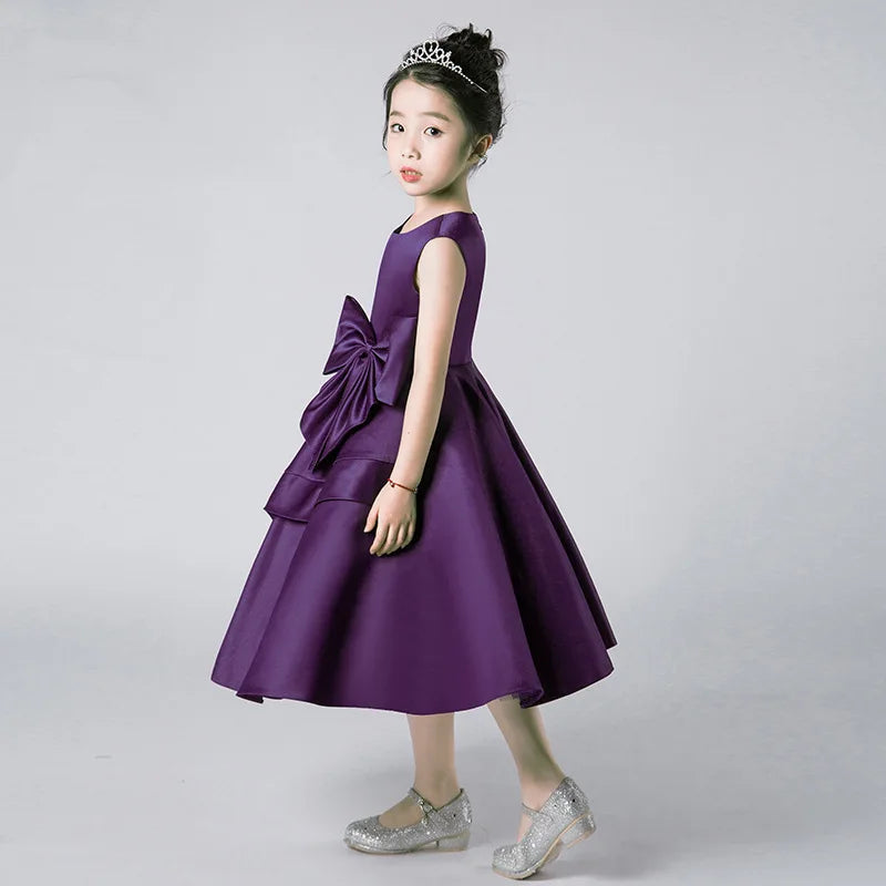 Young girl wearing a purple dress with a large bow on a gray background