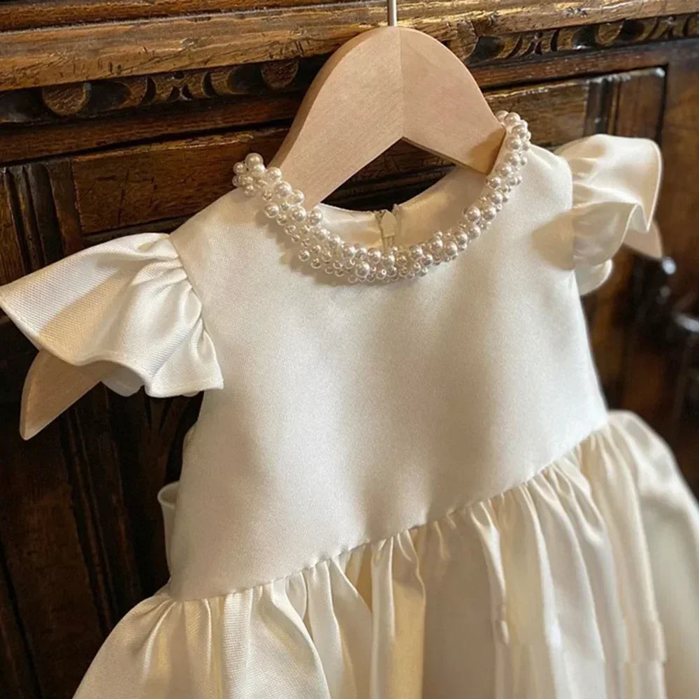 White dress with ruffled sleeves and pearl collar on a wooden hanger against a wooden background